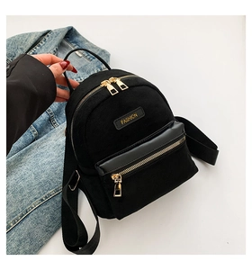 Mini sac à dos noir en toile et cuir avec zips dorés posé sur une veste en jean