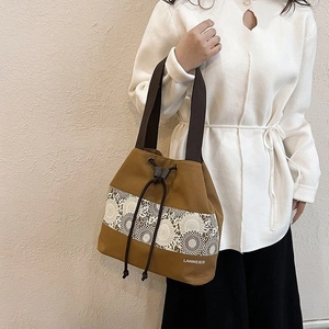 Minimalist brown canvas bucket bag featuring decorative white lace embroidery and drawstring closure
