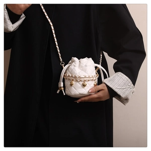 Close-up of white quilted bucket bag with gold heart charms and chain on black coat