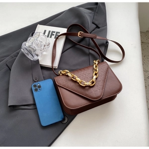 Detail of dark brown crossbody bag with crocodile pattern and golden chain strap
