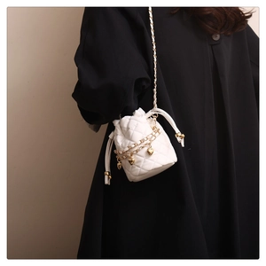 Close-up of a white quilted bucket bag with gold chain and heart charm worn by model