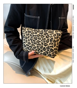 Detailed close-up of a leopard print clutch bag with woven texture held by a model
