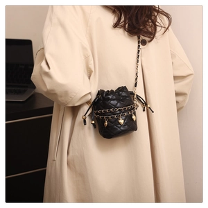 Detail of black quilted bucket bag with gold chain straps and heart charms on a model
