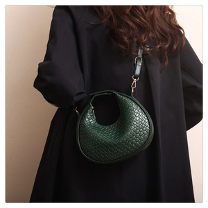 Detailed close-up of dark green woven crescent bag with luxury golden hardware accents