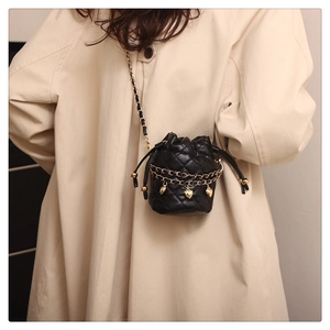 Close-up of black quilted bucket bag with gold chain and heart charm worn by model