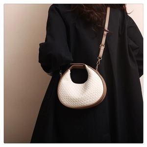 Detail of cream woven crescent bag featuring camel leather trim and adjustable strap