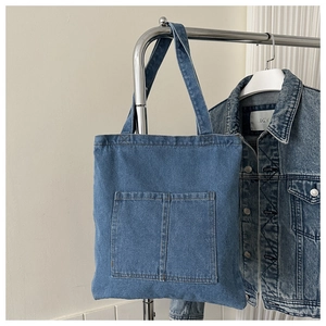 Minimalist denim tote bag with front pockets and wide shoulder straps in blue wash