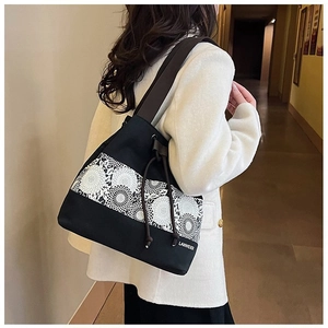 Detail of black canvas bucket bag featuring white floral lace patterns and drawstring closure