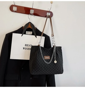 Détail du cabas matelassé noir avec étiquette en cuir marron et chaîne argentée