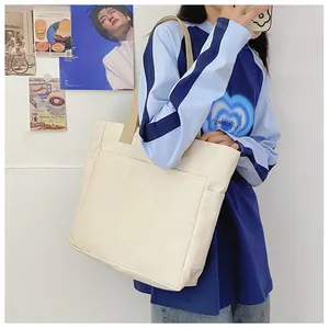 Détail du fourre-tout en toile beige avec poche frontale et bandoulières marron contrastées