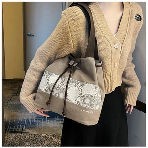 Close-up of khaki canvas drawstring bucket bag with white floral lace pattern and leather straps