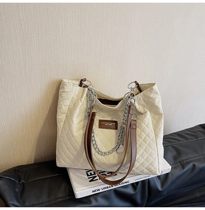 Détail d'un sac cabas matelassé en tissu crème, poignée en cuir marron et chaîne argent