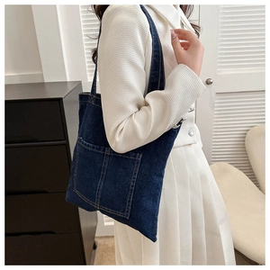 Detail of dark blue denim tote bag featuring contrast stitching and large front pockets