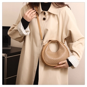 Detail showing khaki woven crescent bag texture with a long trench coat for autumn style