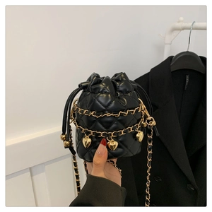 Detailed shot of quilted black bucket bag with golden heart charms and chain strap