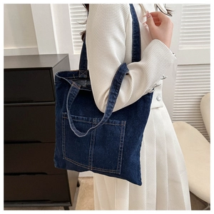 Detail view of navy blue denim tote bag featuring dual front pockets and orange stitching