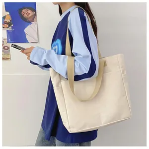 Détail d'un sac cabas en toile blanc cassé avec bandoulière kaki sur l'épaule du mannequin