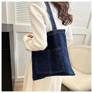 Minimalist deep blue denim tote bag with dual front pockets worn over the shoulder