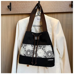 Detail of black canvas bucket bag featuring white floral lace panel and brown strap