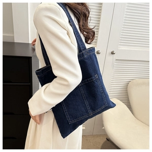 Detail of blue denim tote bag featuring dual front pockets and yellow stitching highlights