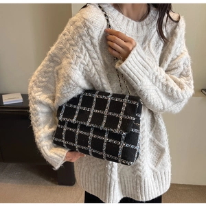 Détail d'un sac à carreaux en tweed bleu avec bandoulière chaîne sur un modèle en pull
