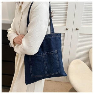 Detail of dark blue denim tote bag with dual front pockets and yellow topstitching details