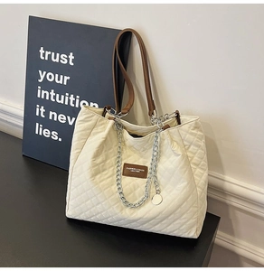 Détail du sac cabas beige matelassé avec lanières en cuir marron et chaîne en métal argenté