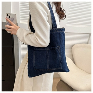 Detail of deep blue denim tote bag featuring dual front pockets and stitched texture