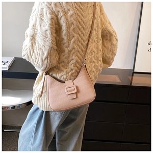 Detail of a light pink crocodile texture crossbody bag worn by a model in soft indoor light