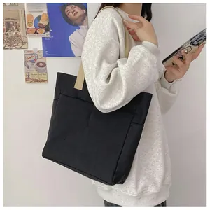 Détail d'un sac cabas noir en toile avec poche avant et anses beiges contrastées