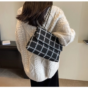 Détail d'un sac bandoulière en tweed noir avec chaîne porté sur un pull blanc