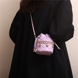 Quilted light purple bucket bag with gold chain strap and heart pendants on black coat