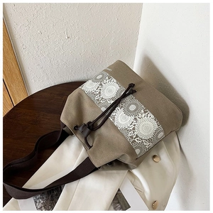 Close-up of khaki canvas bucket bag featuring white floral lace prints and drawstring