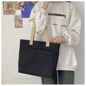 Détail d'un sac cabas en toile avec corps noir, anses blanc cassé et poche latérale pratique