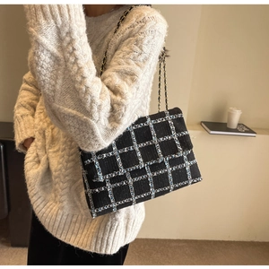 Détail d'un sac à bandoulière en tweed noir avec chaîne dorée sur un pull blanc