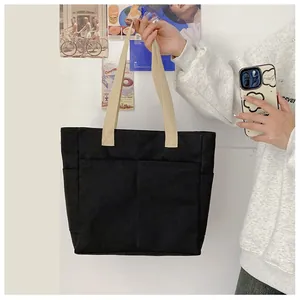 Détail du sac cabas en toile noire avec poignées contrastées et une poche frontale
