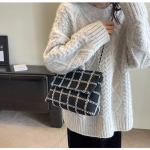 Détail du sac à bandoulière en tweed à carreaux avec chaîne dorée sur un pull blanc élégant