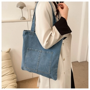 Detail of blue denim tote bag with square front pockets and contrast stitching texture