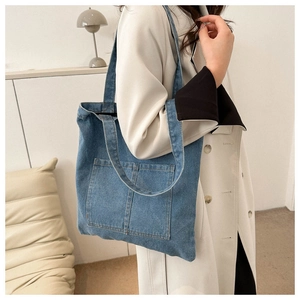 Close-up of blue denim tote bag with two front pockets and soft texture on a shoulder