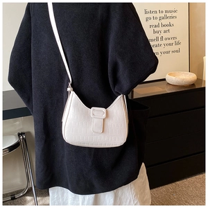 Minimalist white crocodile texture saddle bag shown worn on shoulder in a warm room setting