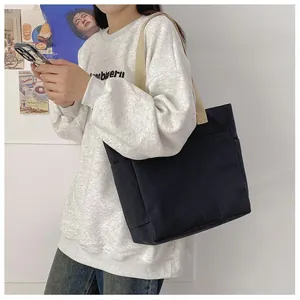 Vue détaillée du grand sac cabas en toile noire avec des anses beiges porté à l'épaule