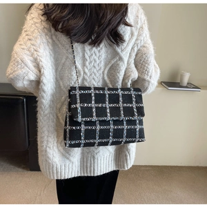 Détail d'un sac à bandoulière en tweed noir à carreaux avec chaîne et fils bleus