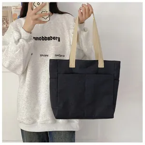 Détail d'un sac cabas en toile noire avec grandes poches avant et anses en ruban beige