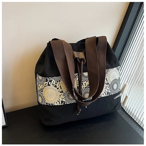Close-up of black canvas bucket bag featuring floral embroidery and brown woven straps