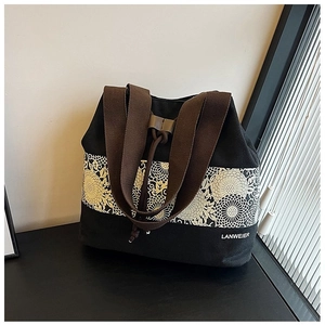 Detail of black canvas bucket bag with floral embroidery and brown woven shoulder strap