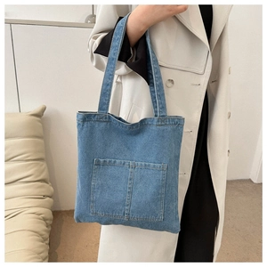 Detail of light blue denim tote bag with two front patch pockets and durable canvas texture