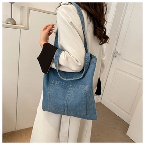 Detailed close-up of blue denim tote bag featuring dual front pockets and wide shoulder strap