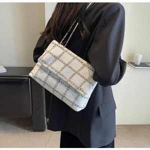 Sac à bandoulière en tweed à carreaux avec chaîne en métal porté par un mannequin en intérieur