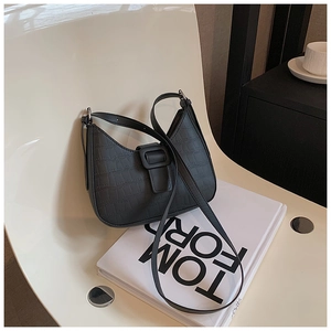 Close-up of black crocodile pattern leather bag with silver buckle on a minimalist chair