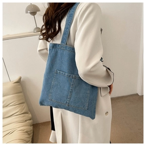 Detail view of blue denim tote bag featuring dual front square pockets and wide shoulder strap